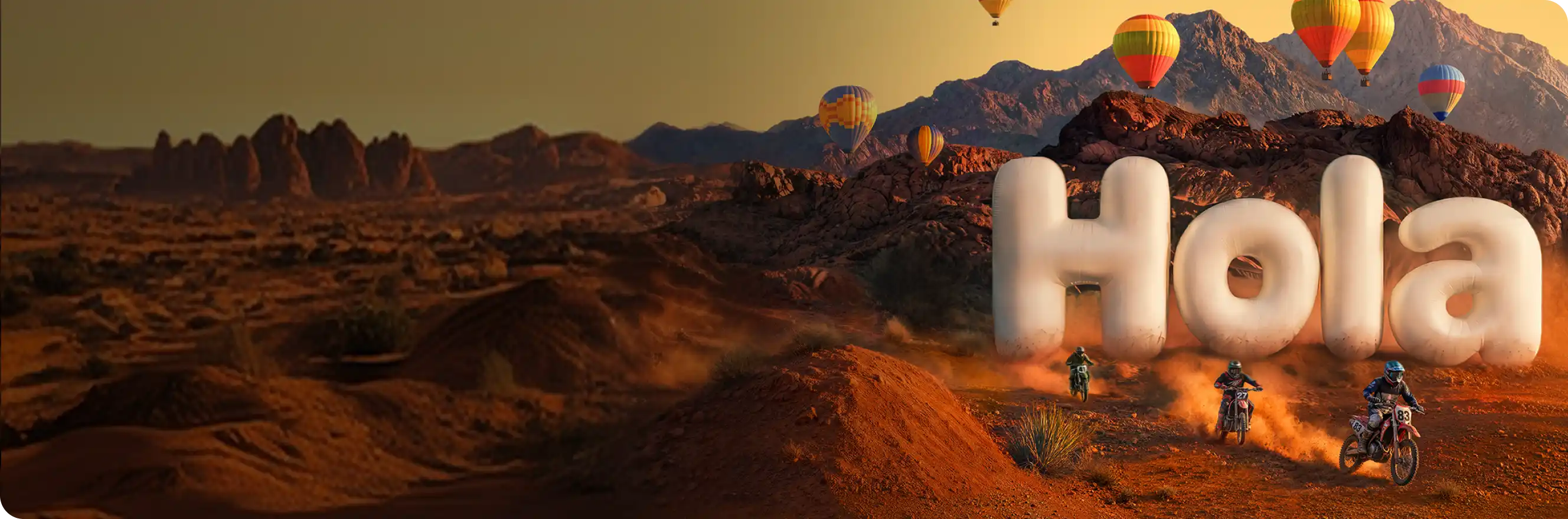Ciclistas de motocross subiendo por un sendero en el desierto, alejándose de unas letras gigantes inflables que forman la palabra "¡Hola!", mientras globos aerostáticos de colores flotan sobre montañas rocosas.